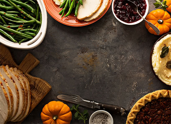Top down view of a Thanksgiving spread of multiple dishes on a dark, tabletop