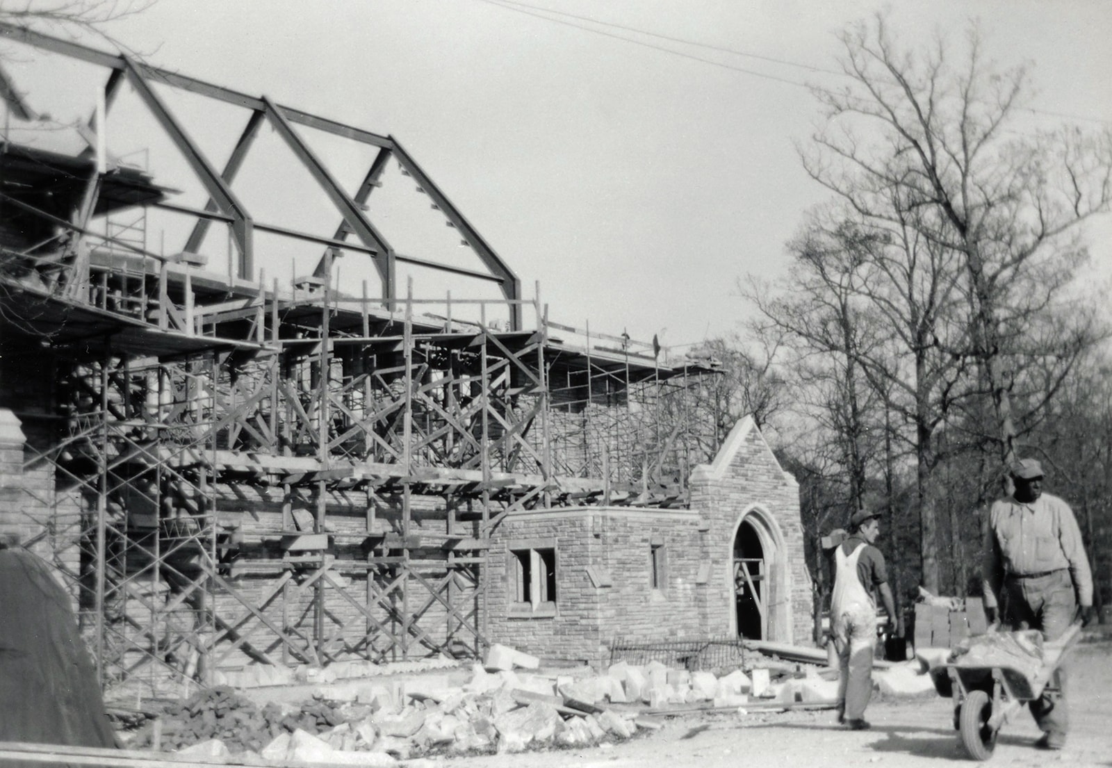 Black and white photo of two workers pushing wheelbarrows and surveying the site of a Alumni Memorial Chapel during its construction