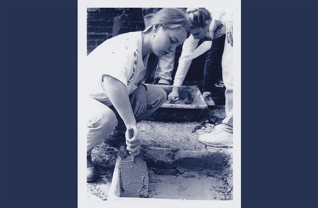 Black and white photo of a student kneeling down to scoop grout