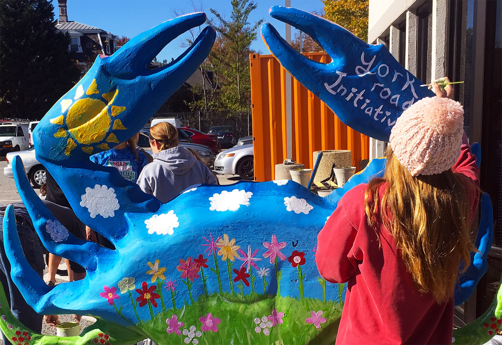 Students painting a large statue of a crab with bright colors that read 'York Road Initiative' outside on a sunny day