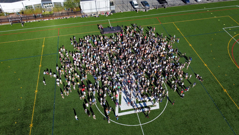 A large group of first-year students gathers on a field during a Fall Welcome Weekend activity