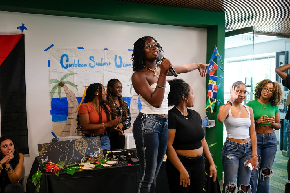 A student speaks into a microphone while introducing the Caribbean Student Union at the Thrive Center Block Party