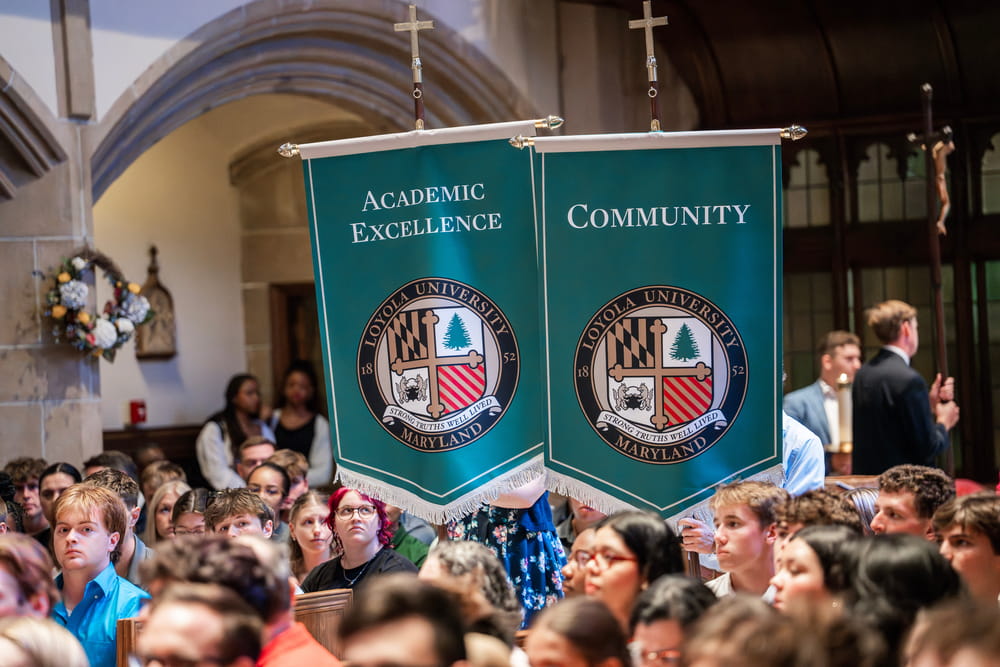 Banners reading “Academic Excellence” and “Community” are carried through a crowd during the opening procession of Loyola’s Mass of the Holy Spirit