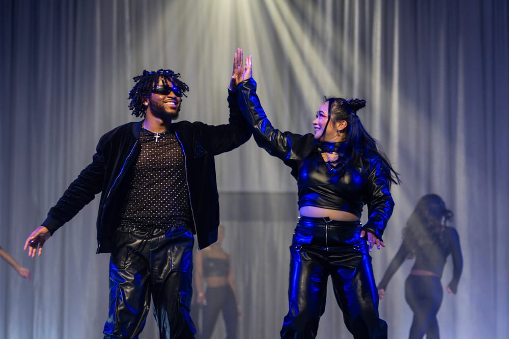 Two students high-five on stage and under spotlights at the annual Black Student Association Fashion Show.
