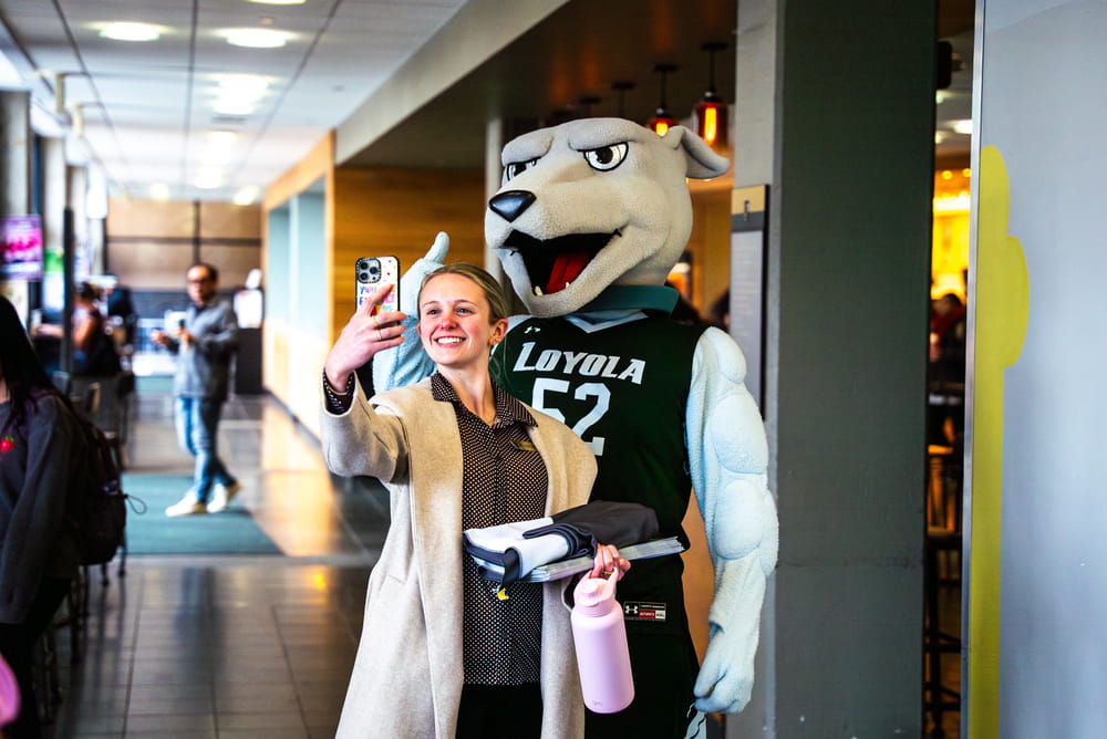 A student posing with Iggy, the Loyola Greyhound mascot, holding her phone out for a selfie
