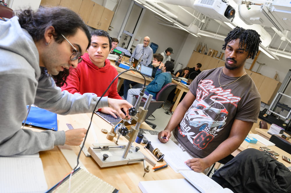 Four students conduct a hands-on engineering experiment around a lab table with equipment and a prototype