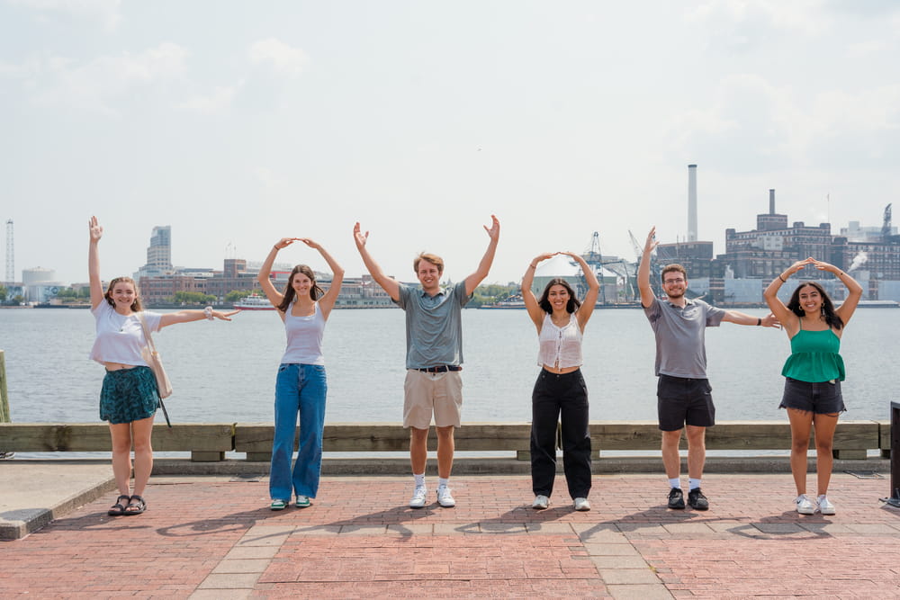 Students stand by Baltimore's waterfront in Fell's Point and spell out L-O-Y-O-L-A with their arms.