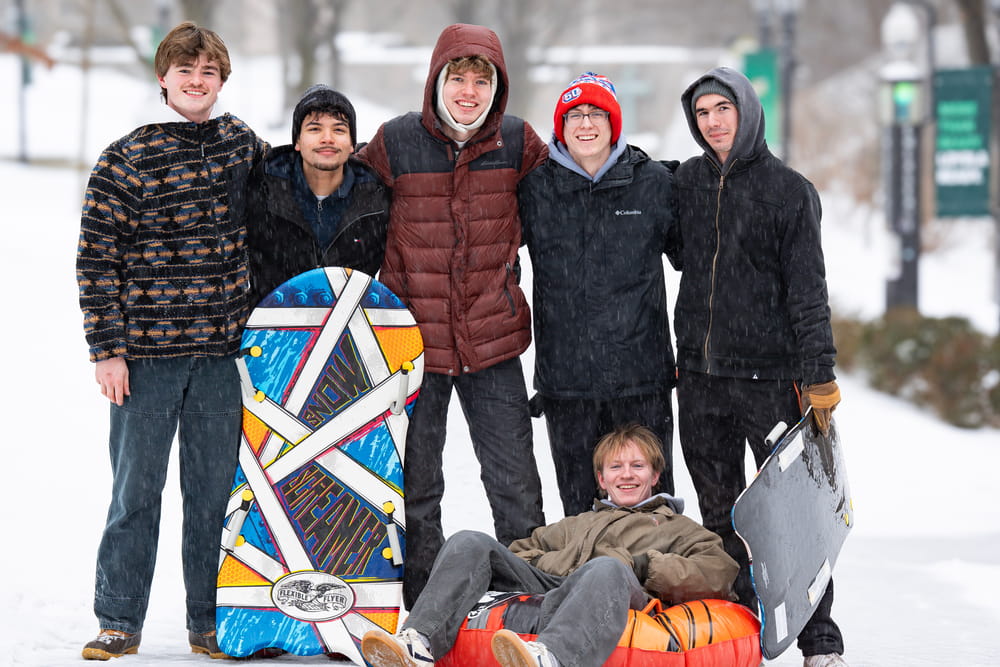 A group of students pose with sleds in front of the snow-covered Quad