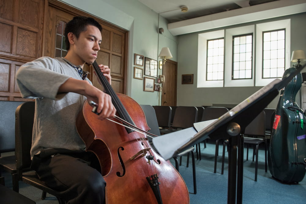 A student reading music as he practices the cello.