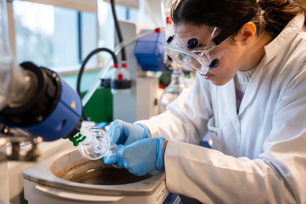 A student in a lab coat and goggles conducting an experiment with a specialized piece of chemistry equipment
