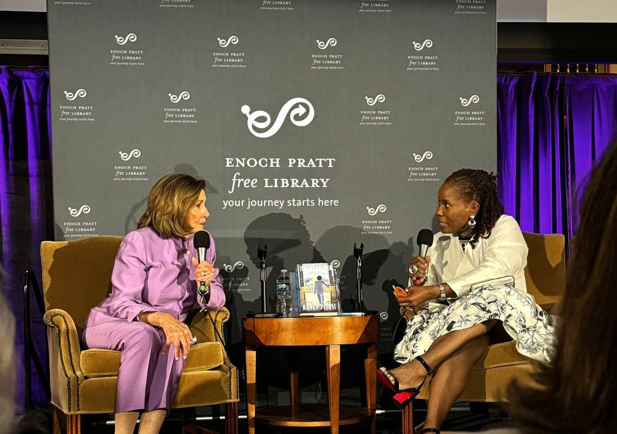 Dr. Whitehead engages in conversation with Nancy Pelosi. They are seated, partially facing each other. Nancy Pelosi's book is on the table between them.