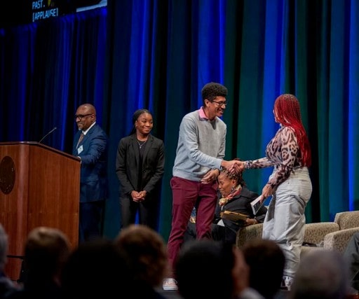 Two students, two faculty members, and an author are on a stage with a podium and two chairs at Loyola University Maryland
