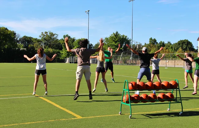 Students doing jumping jacks on an athletic field