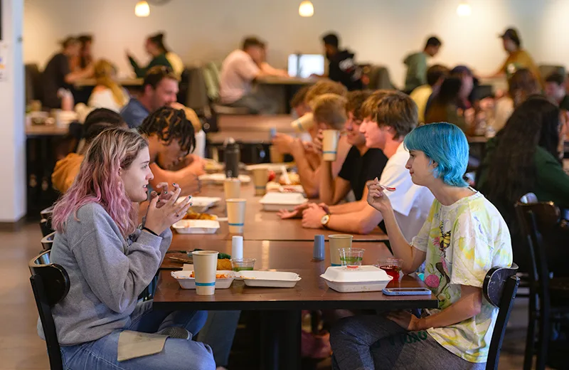 Students sit and eat at tables in a dining hall