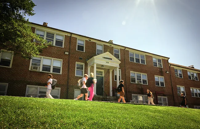 Students walk in front of a red-bricked building on a sunny day