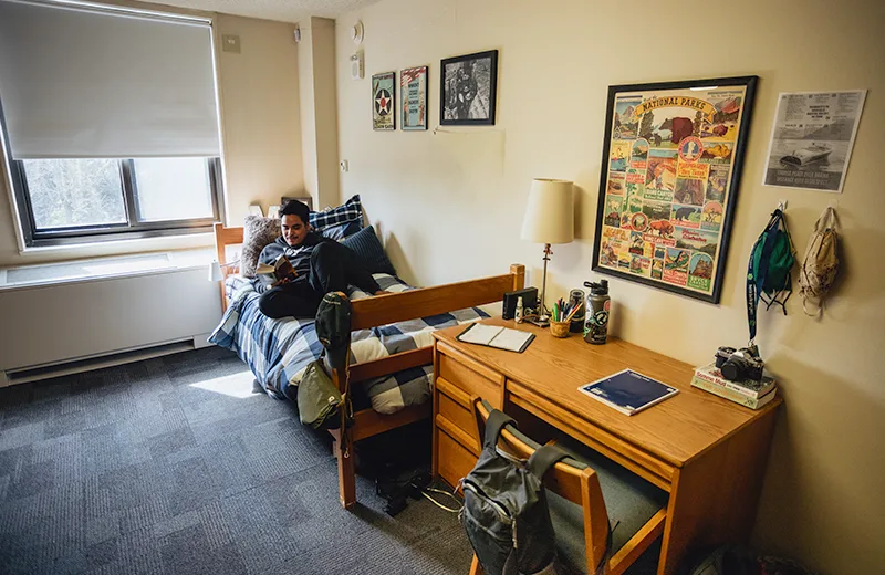 A student sits on his bed while reading a book