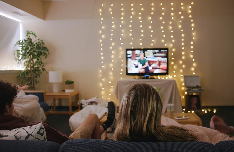 Students watch TV, with Christmas lights on the wall behind it