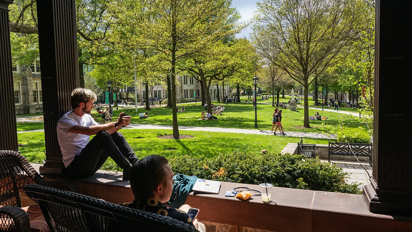 Students sitting on the porch of the Humanities building, looking out toward the green quad - Press enter to play