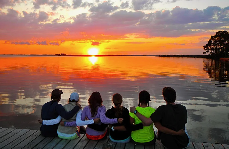 Students sitting on a dock enjoying a bright orange sunset