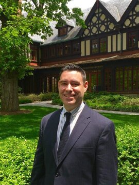 Brian M. Oakes, ’99, MBA ’10, standing in front of the Humanities building on Loyola's evergreen campus