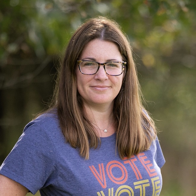 Amy Becker smiles for a posed portrait in a shirt that says, "Vote"