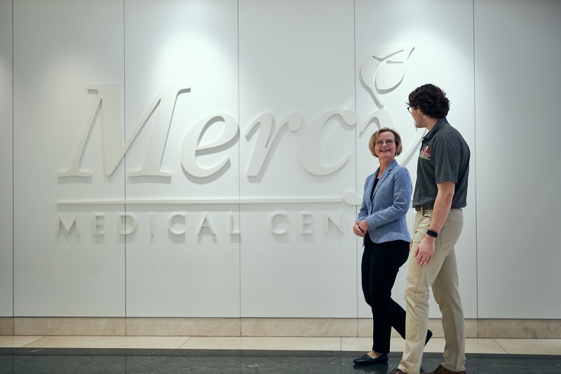 A Loyola faculty member walks with a student past a sign at Mercy Medical Center.