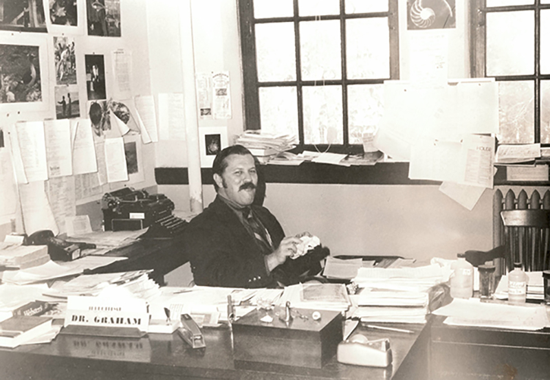 Black and white photo of Graham sitting behind the desk in his office.