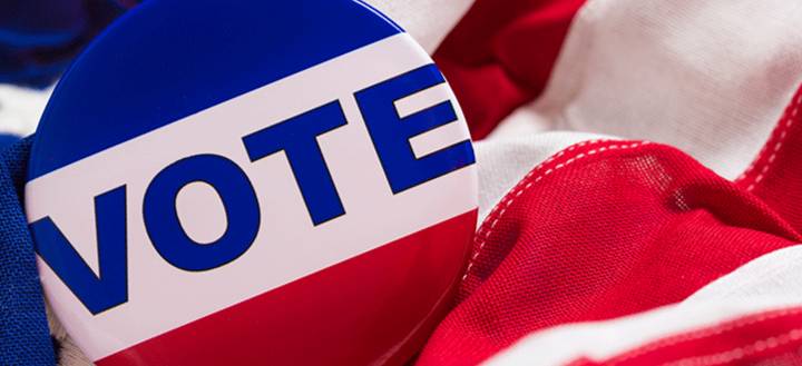 A red, white, and blue "vote" button on an American flag.