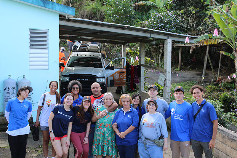 Loyola students, Let's Share the Sun members, and the project beneficiary, Rosa, pose for a photo outside of her house following the solar panel installation.