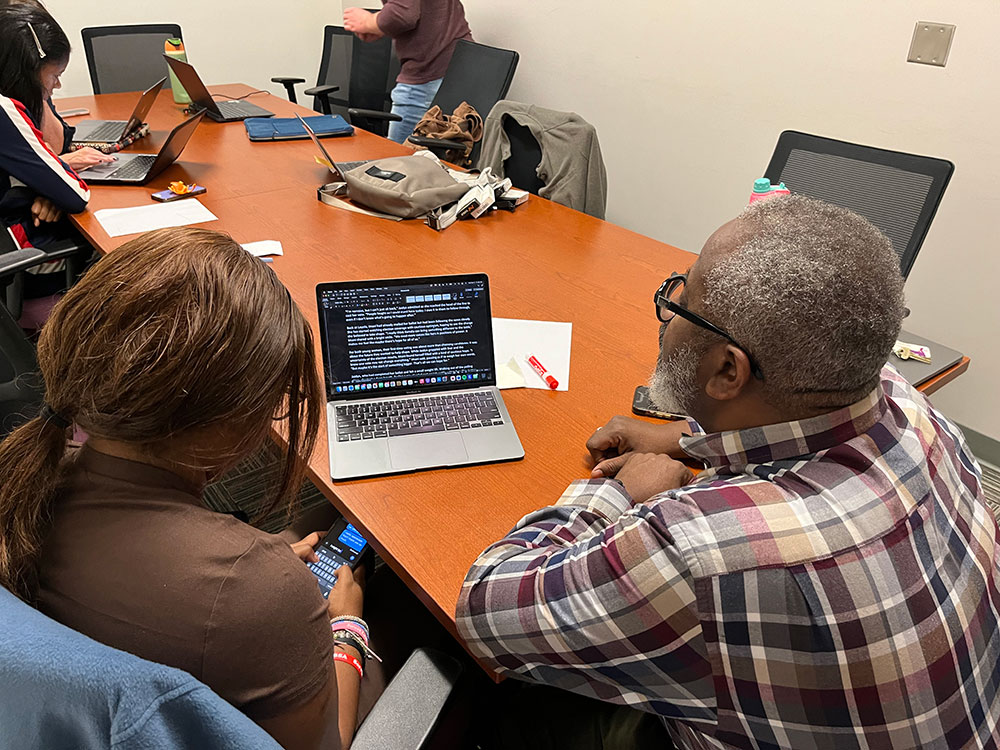 Dr. Tooten sits with a student at a conference table with a laptop. Dr. Tooten volunteered his time to work with journalism students to cover the 2024 presidential election. (Photo: Sara Magee, Ph.D., associate professor of communication and media)