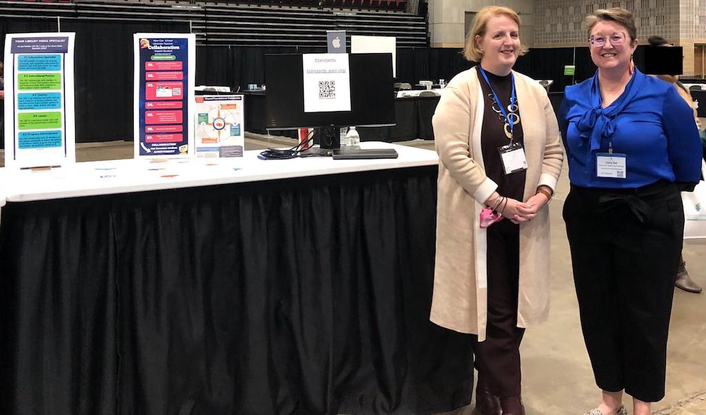 two women with conference nametags standing at a table with a research poster