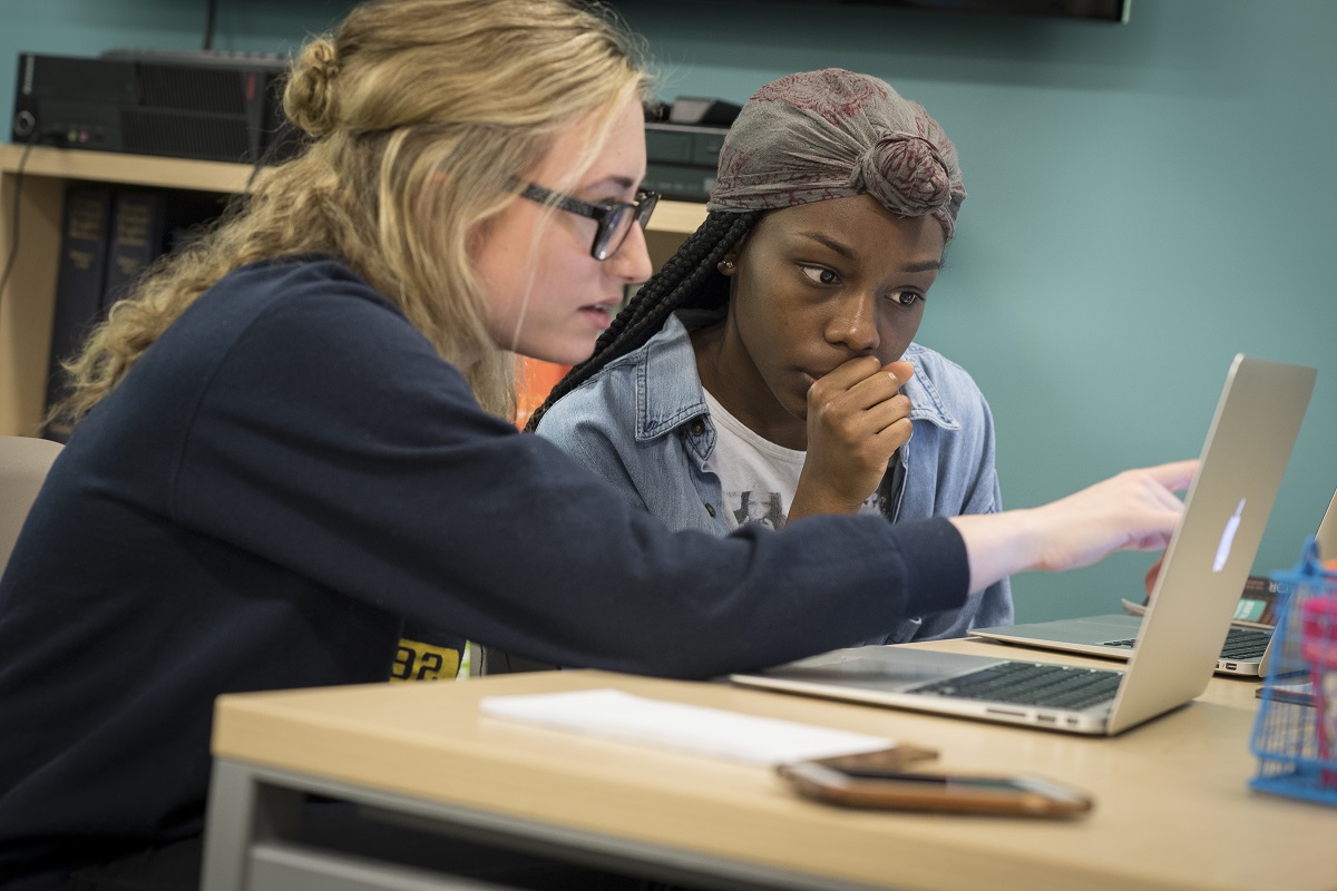 Two students work together on a laptop, one points at the screen