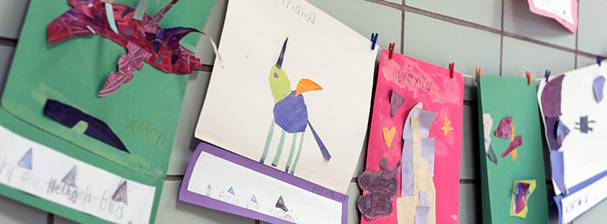 Elementary student artwork on construction paper hanging up in a school hallway