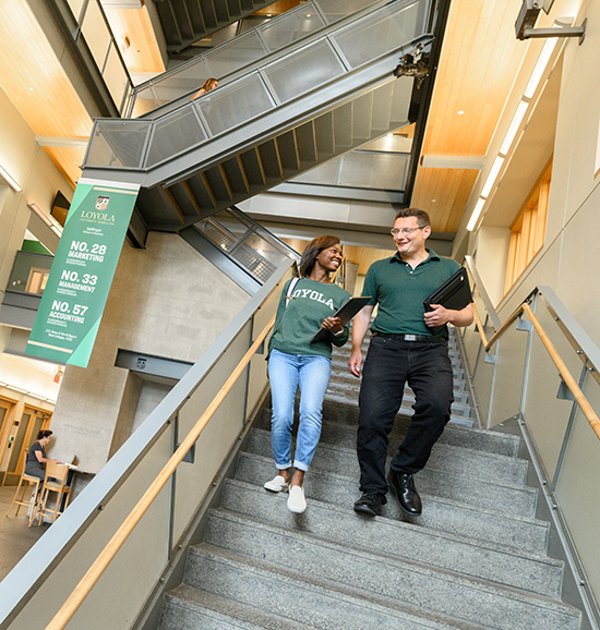 Two Loyola University Maryland accounting students walking down the Sellinger School of Business stairwell while discussing coursework and carrying laptops.