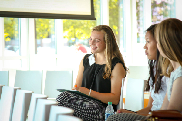 a group of students sit smiling in a room with lots of windows