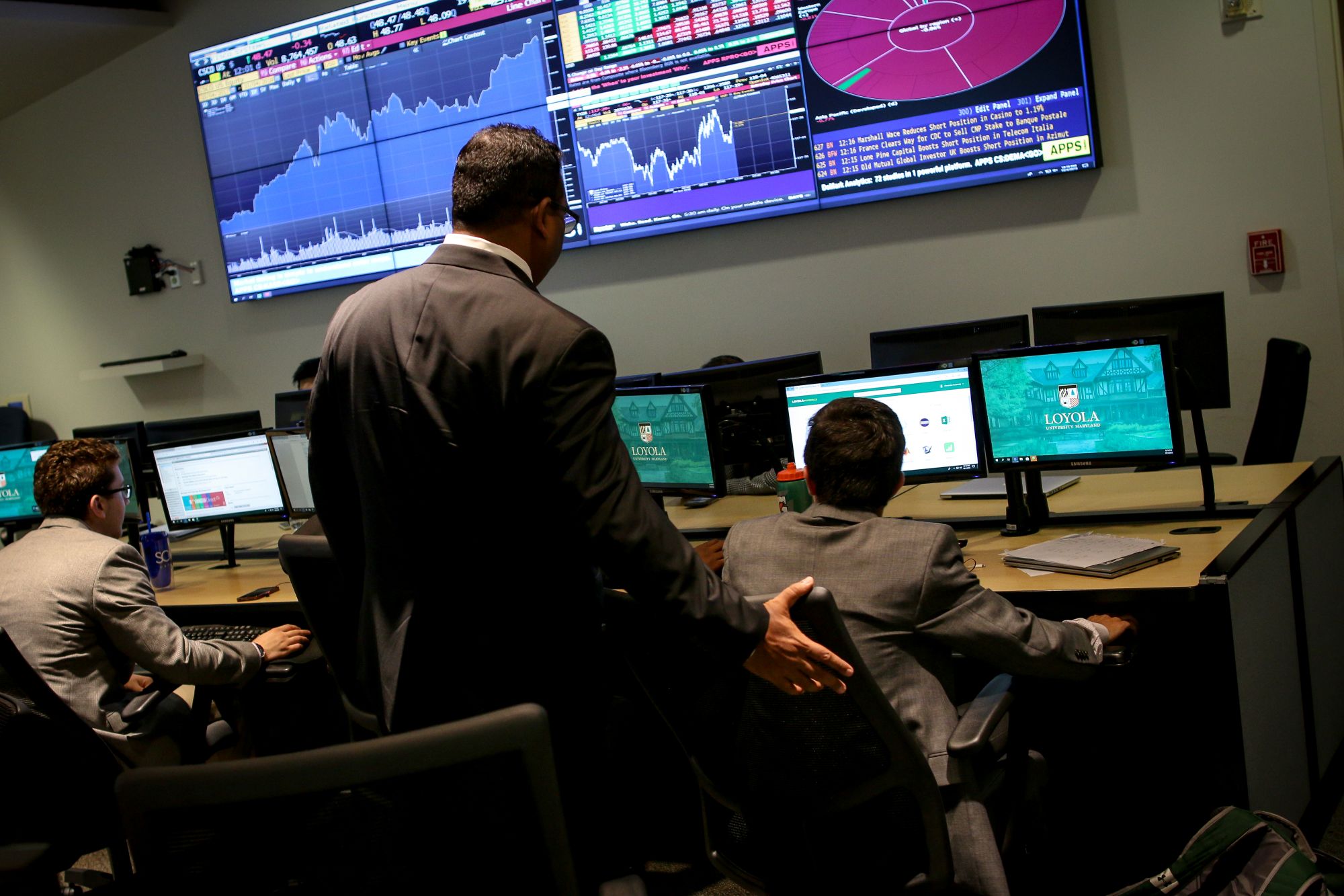 men in suits look at computer screens with graphs and charts
