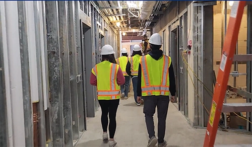 People walk through construction site with vests and hardhats