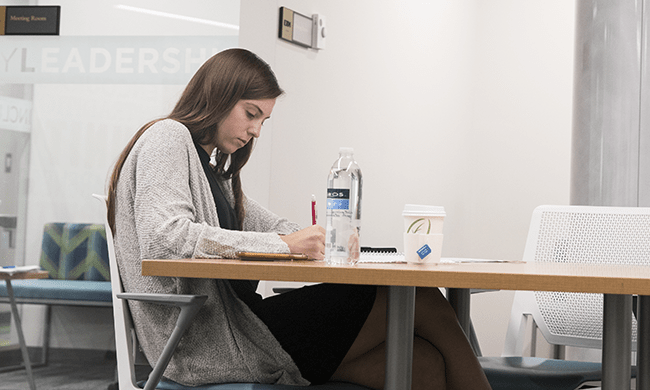 A student writes at a desk in a well-lit study area